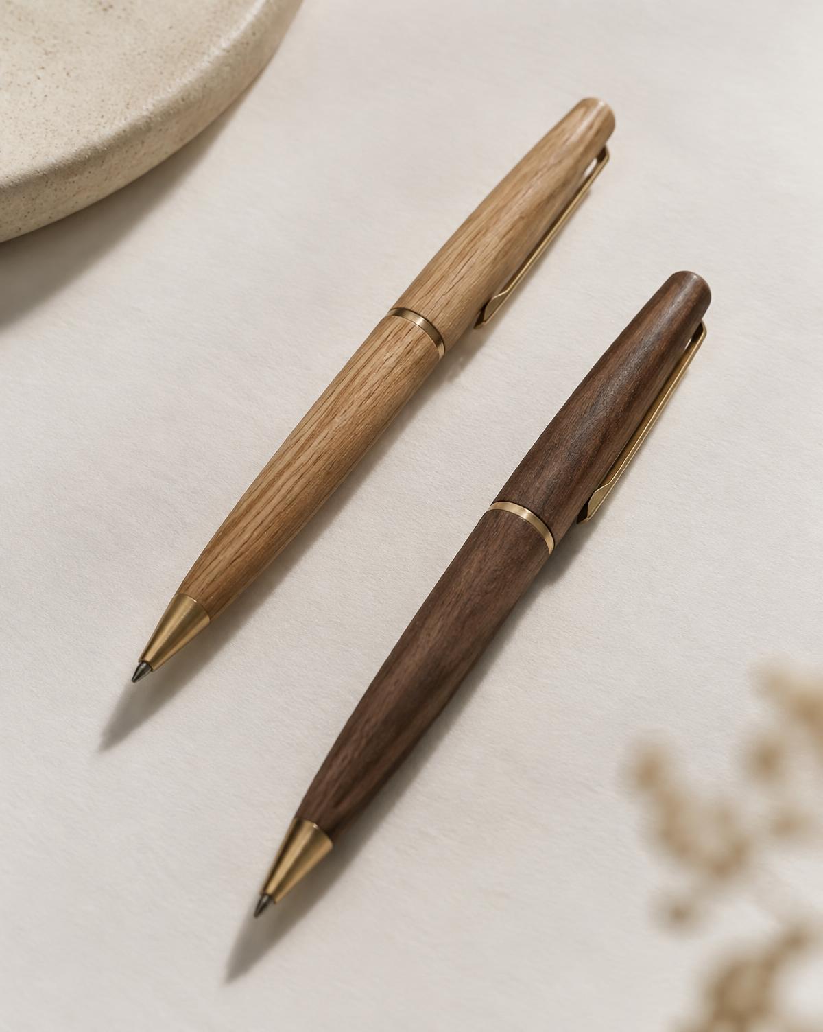 Two slim handcrafted wooden pens in oak and walnut on pale paper